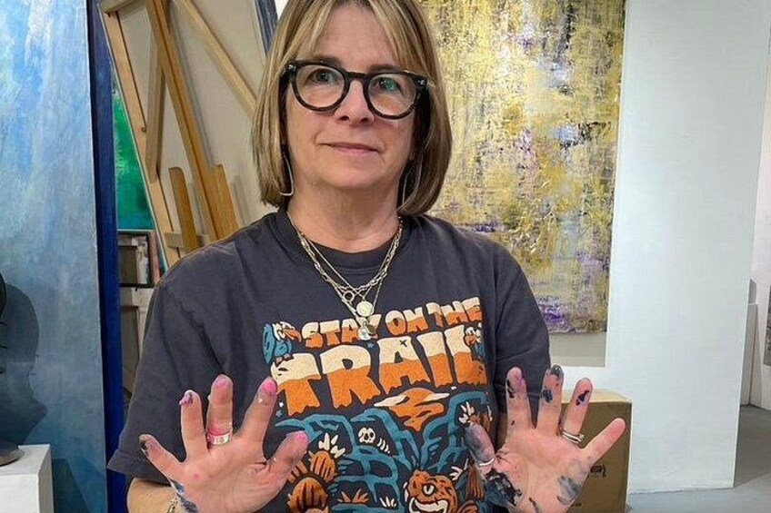 A person wearing a t-shirt with a colorful graphic design, standing in an indoor setting with a painting in the background. 3