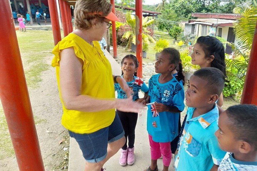 Una mujer con blusa amarilla y shorts vaqueros interactúa con niños en un parque infantil con pilares rojos. 2