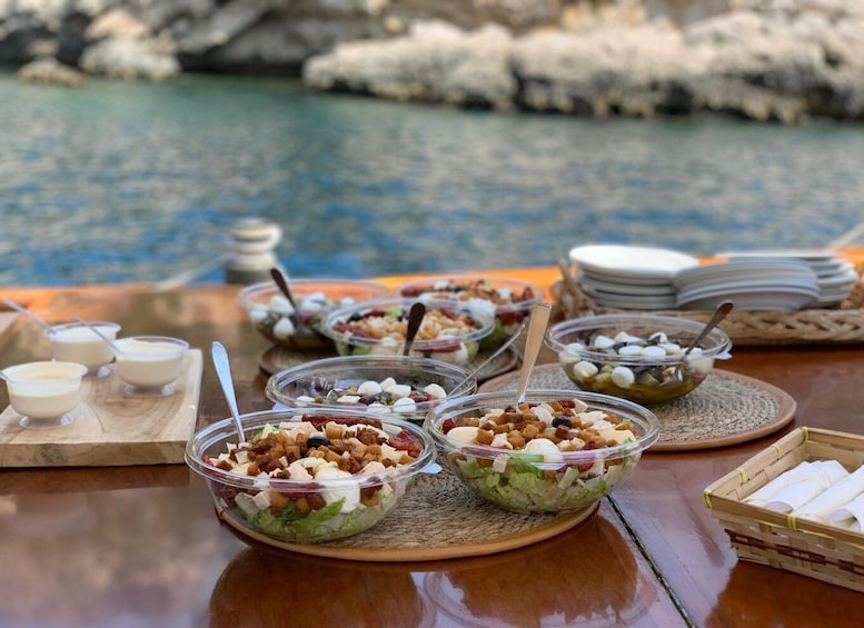 Une table dressée avec divers aliments et des bols, le tout placé sur un fond constitué d’une côte rocheuse et de l’eau. 2