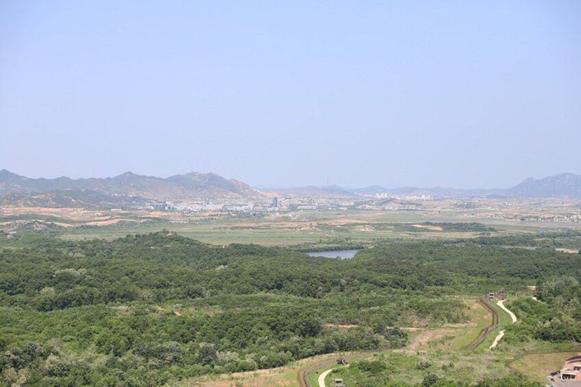 A landscape with a winding road, dense greenery, a small body of water, and distant mountains. 2