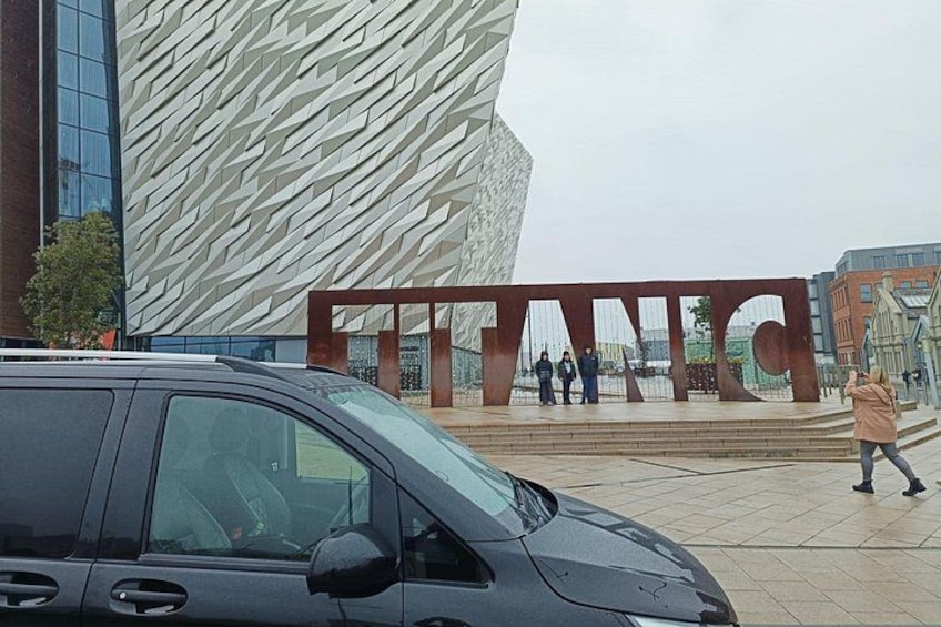 A modern building with a distinctive geometric facade and a large sign with the word 'TITANIC' in the background. 5