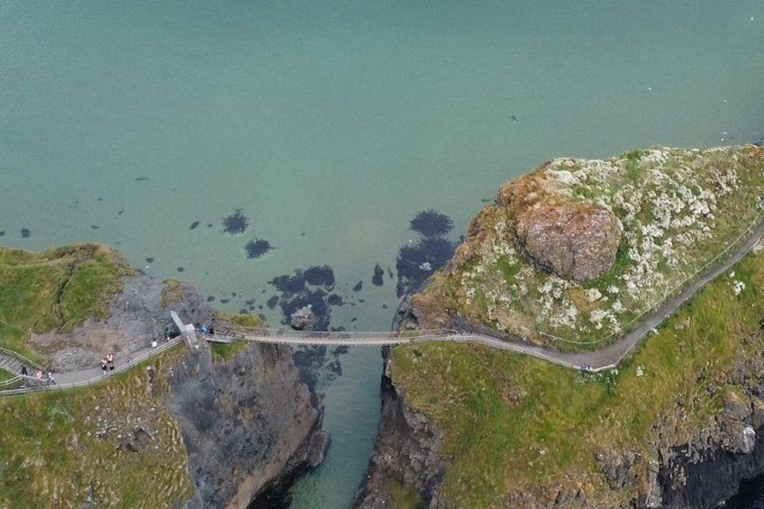 A suspension bridge over a narrow water gap, surrounded by rocky cliffs and grassy areas. 1