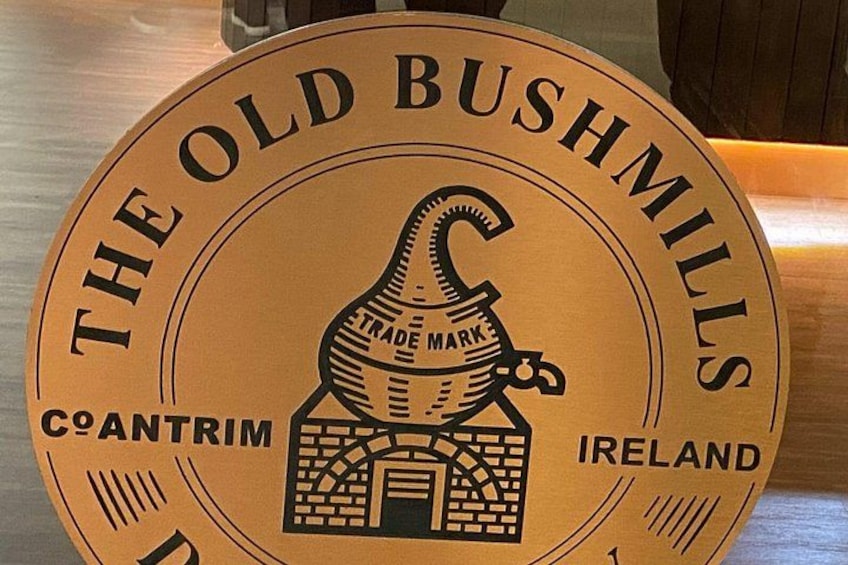 A circular sign with 'THE OLD BUSHMILLS' text, a trade mark symbol, and a building illustration. 3