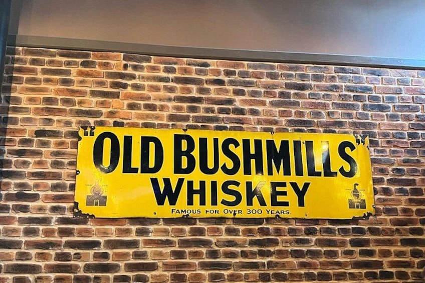 A yellow sign on a brick wall advertising Old Bushmills Whiskey, claiming fame for over 300 years. 2