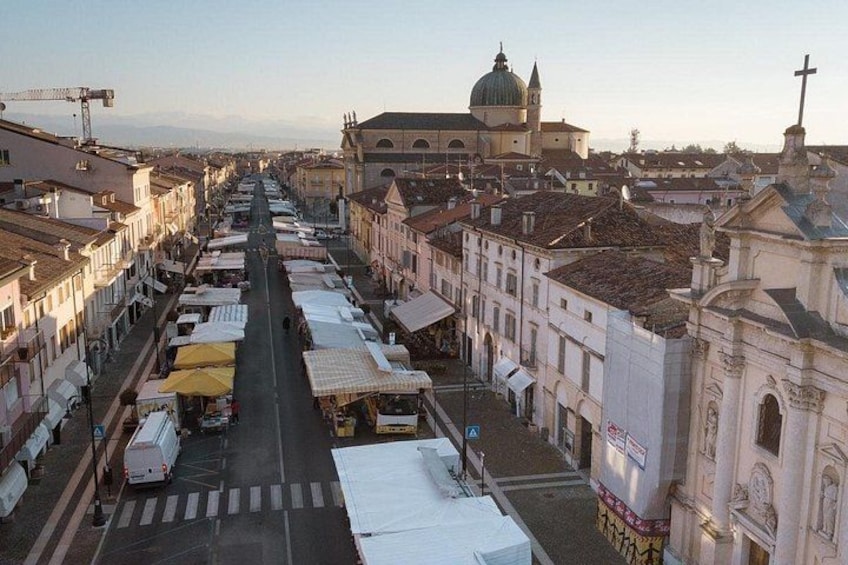 Eine Straße mit Marktständen und Gebäuden, eine markante Kirche mit einer Kuppel und einem Kreuz an einem Gebäude. 3