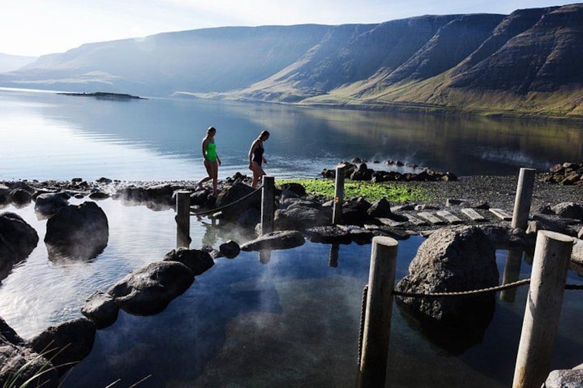 A lake with rocky shores, two people standing on a wooden platform, and mountains in the background. 2