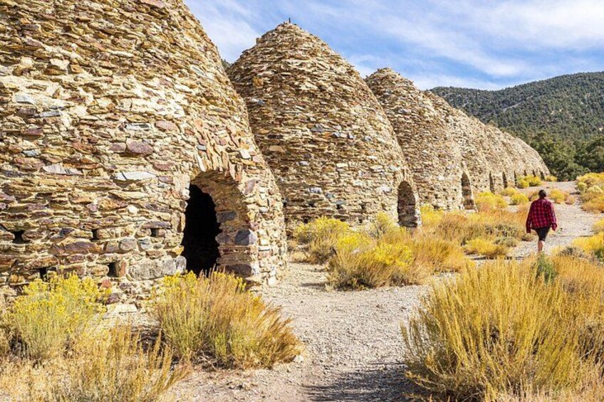 A stone structure with arches, a person walking, and a mountainous landscape. 3