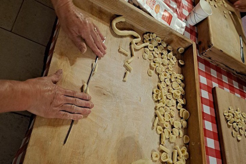 Hands shaping dough on a wooden board, with a checkered tablecloth and a bag of flour in the background. 3