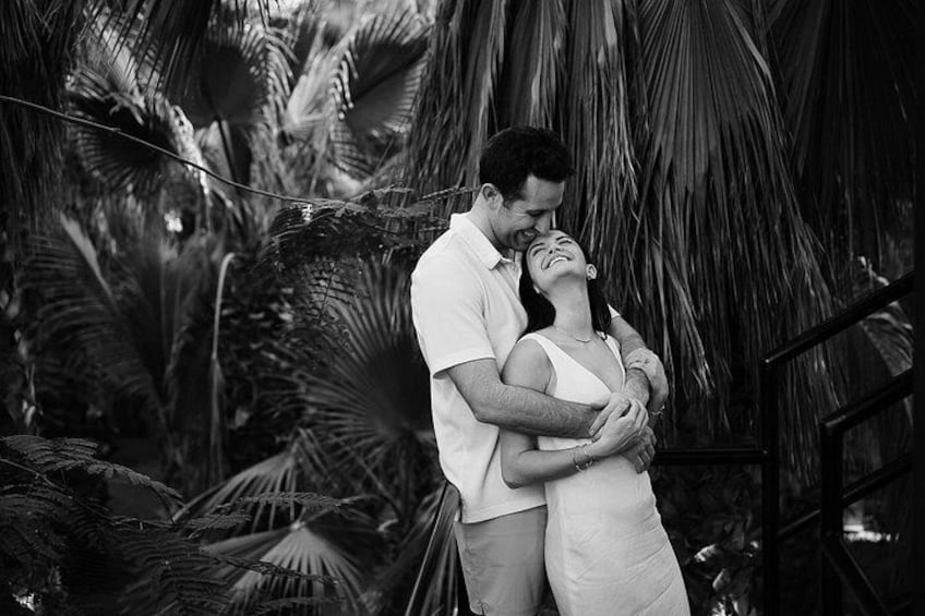 A couple embracing in a tropical setting with palm trees and a thatched structure in the background. 4