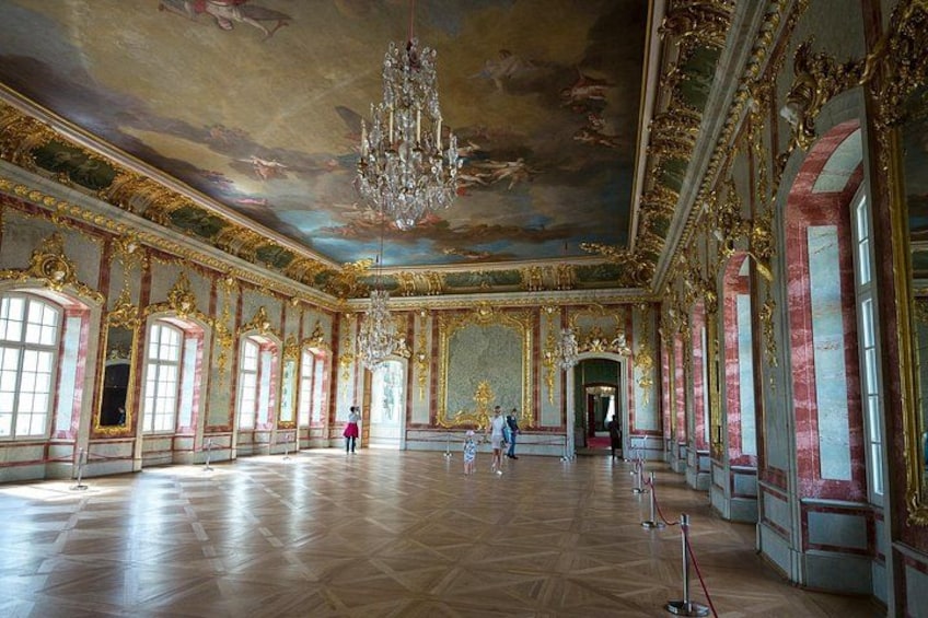 An ornate room with a large chandelier, red and gold decorations, and a polished wooden floor. 1
