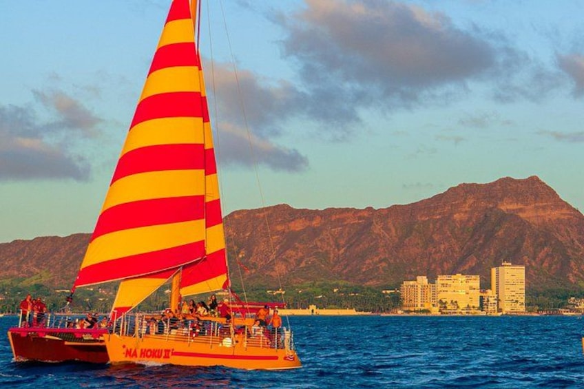 Un velero con vela a rayas rojas y amarillas, un paisaje urbano con edificios y una cadena montañosa al fondo. 2