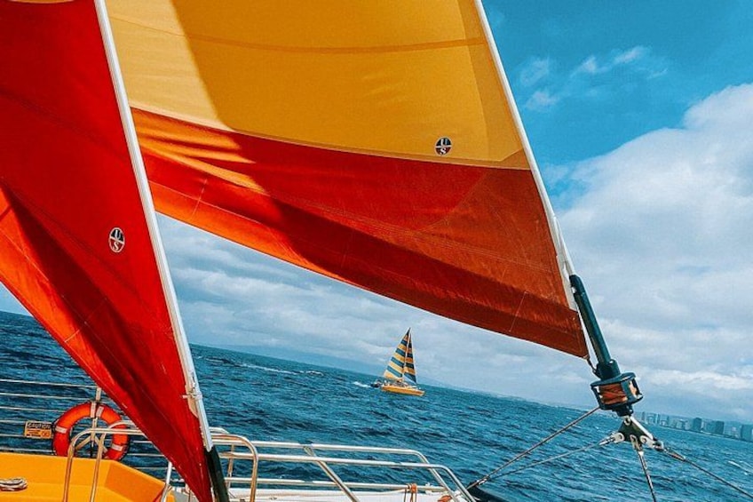 Un velero con velas rojas y amarillas, un flotador salvavidas y un velero amarillo distante en el agua. 3