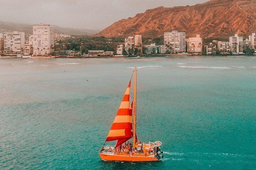 Un velero con una vela multicolora sobre aguas turquesas, una silueta urbana y una montaña al fondo. 4