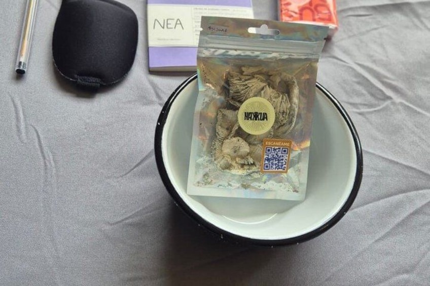 En svart väska, en penna, en bok och ett paket med torkad svamp ligger på ett bord. 2
