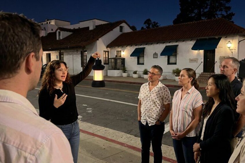 A group of people standing on a street at dusk, with a building in the background. 1