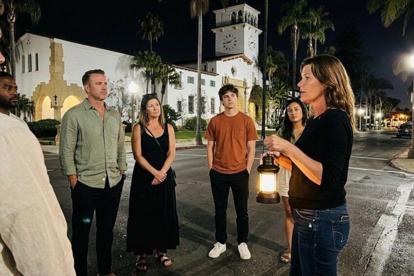 A group of people standing on a street at night with a clock tower in the background. 4