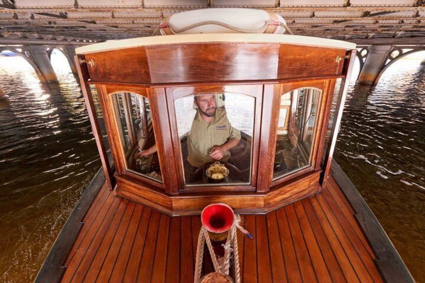 A wooden boat with a cabin, a person steering, and a rope tied to the front. 5