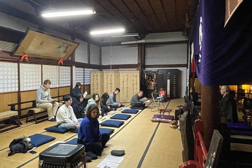 Une pièce avec des tatamis où des personnes sont assises sur des coussins, une pièce de style japonais traditionnel avec un sol recouvert de tatamis, et un paravent shoji en arrière-plan. 2