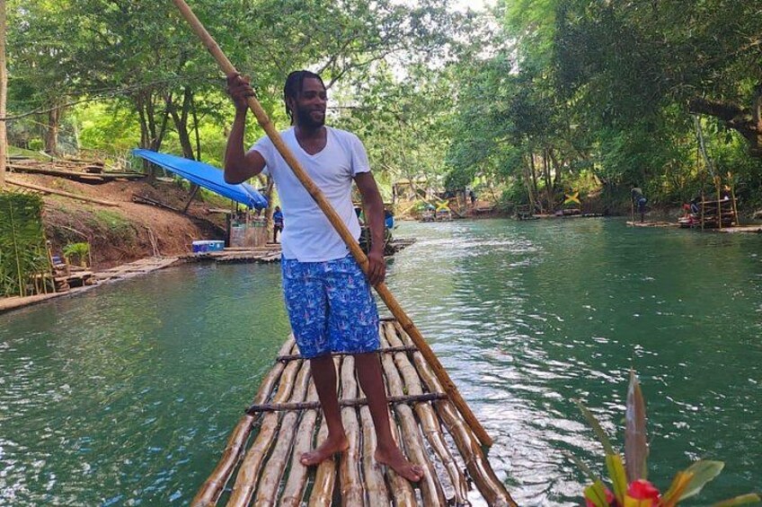 A person standing on a bamboo raft in a river surrounded by greenery. 1