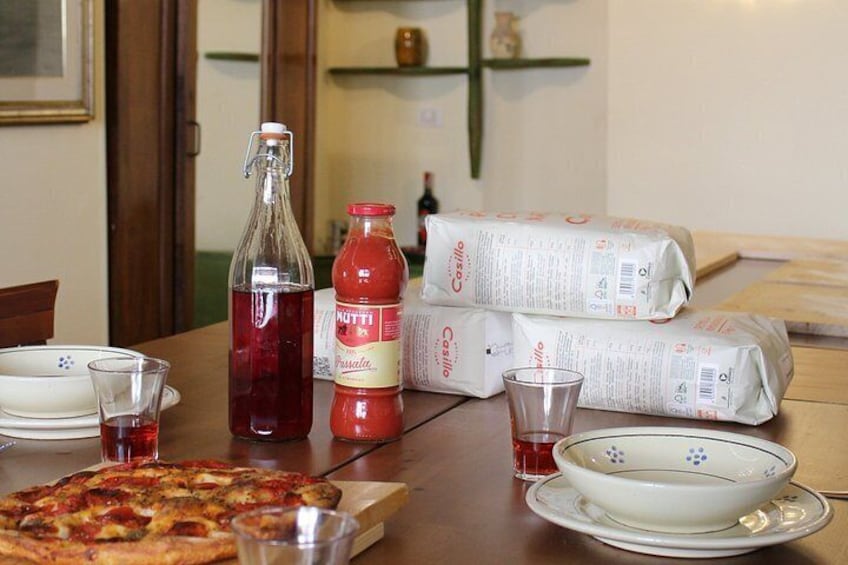 A table with a pizza, a bottle of red liquid, a bottle of ketchup, and packets of pasta. 2