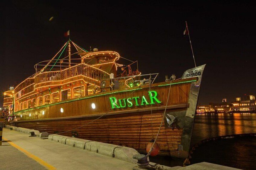 A wooden boat named RUSTAR docked at a pier with city lights in the background. 2