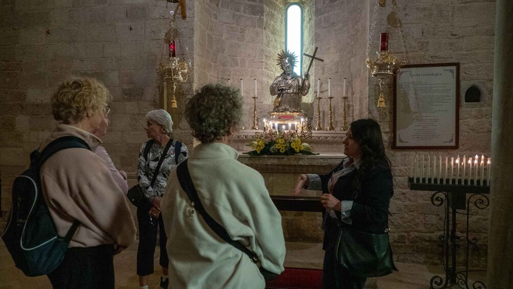 A group of people in a church with a statue of a figure holding a cross, candles, and a framed document on the wall. 5