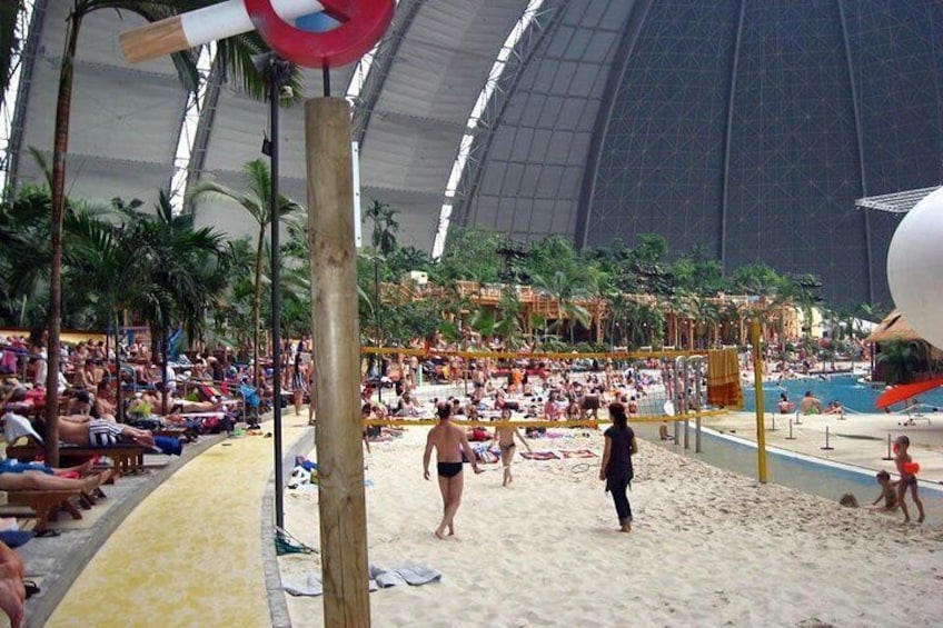 An indoor beach with people sunbathing, a volleyball net, and a large dome structure. 3