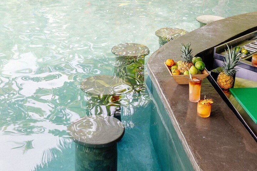 En pool med ett område där man kan beställa drinkar, samt ett utbud av frukt och andra drycker. 5