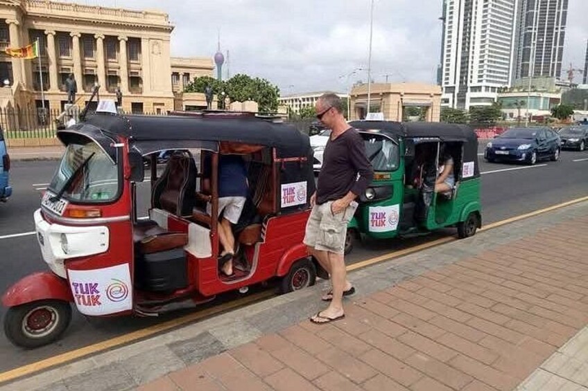 Twee tuk-tuks staan langs de kant van de weg, met een man die erbij staat. 2