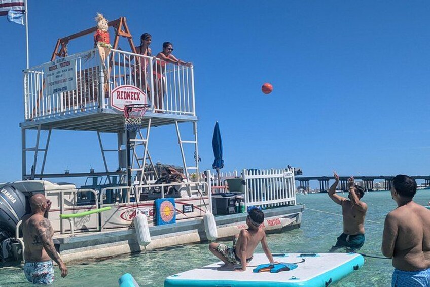 A beach volleyball game with a lifeguard tower, a pier, and a boat in the background. 1