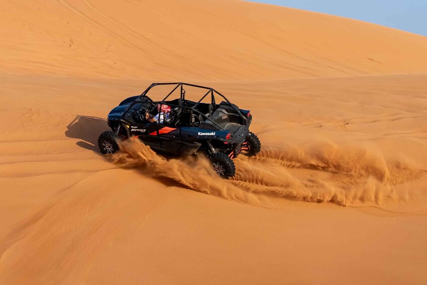 A blue off-road vehicle driving through a desert with sand being kicked up behind it. 4