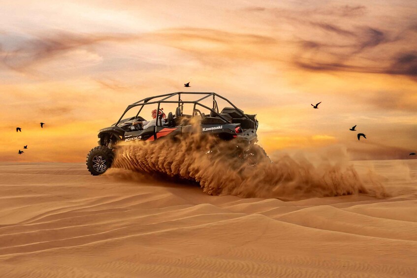 A Kawasaki ATV in a desert with sand being kicked up by its tires. 1