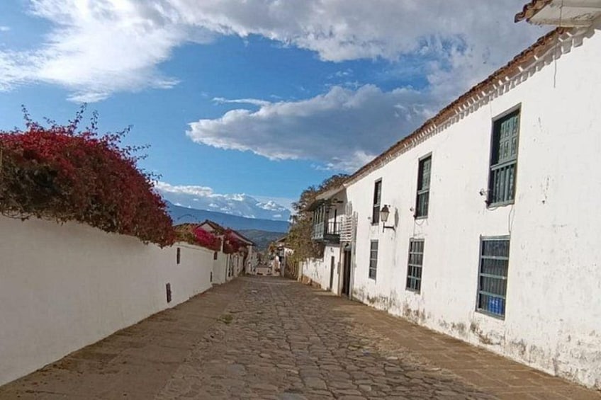 A cobblestone street lined with white buildings, red flowers on the left wall, and a clear blue sky. 2
