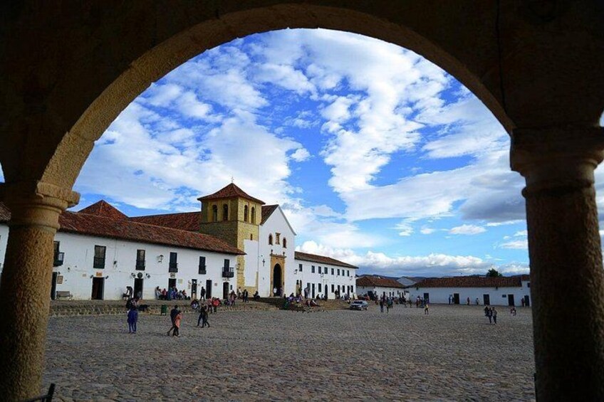 A historical square with white buildings, a prominent church with a bell tower, and an open sky. 2