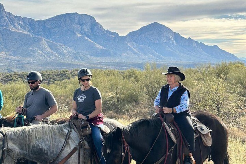 Tres personas montando a caballo en un paisaje desértico con montañas al fondo. 3