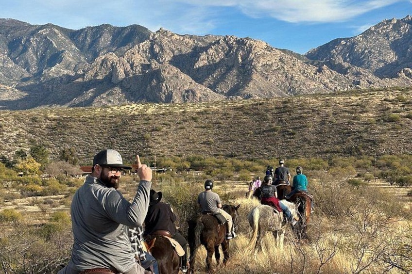 A group of people riding horses on a trail with mountains in the background. 4