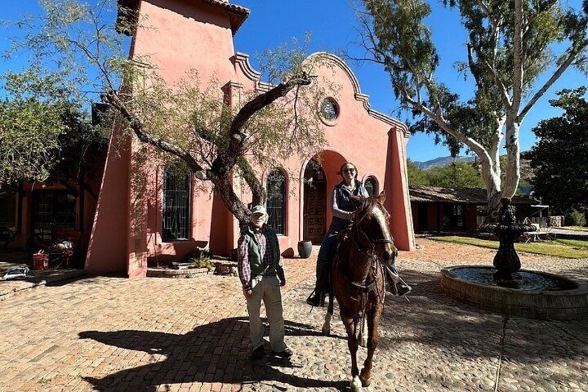 Una persona a caballo frente a un edificio rojo con ventanas de arco y un campanario. 4
