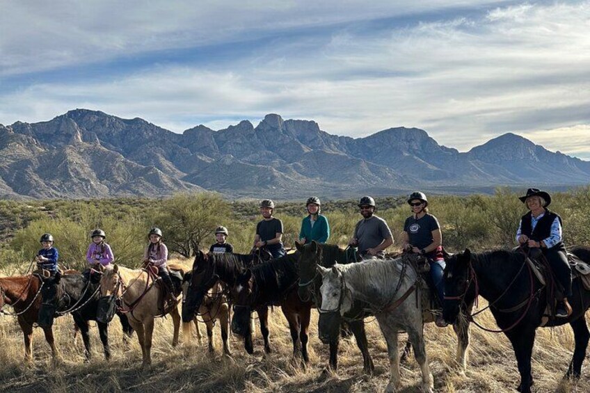 A group of people riding horses across a grassy field with mountains in the background. 1