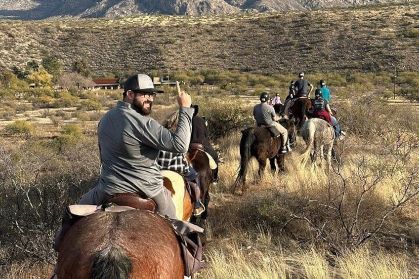 Un grupo de personas montando a caballo en un paisaje desértico con vegetación escasa y montañas al fondo. 2