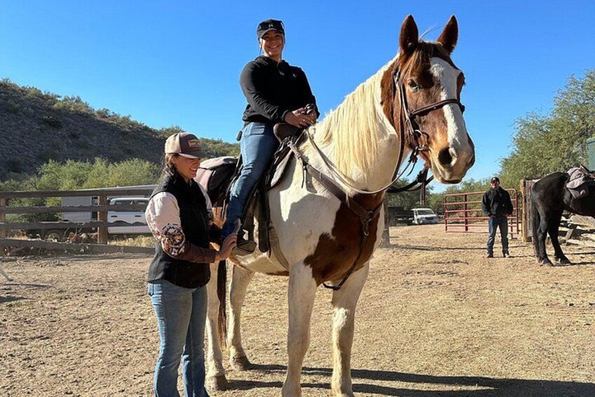 A person riding a horse in an outdoor arena with another person standing nearby. 2