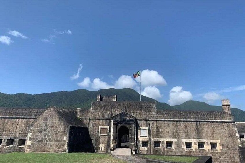 Un bâtiment en pierre, orné d’un drapeau, doté d’une grande entrée et situé dans un paysage montagneux. 1