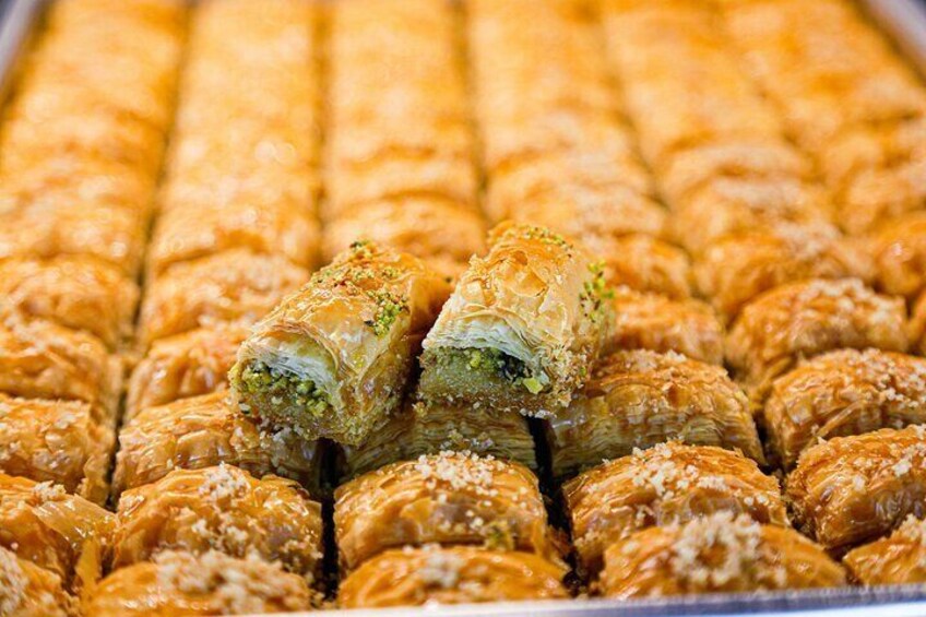 Una bandeja de baklava con textura escamosa de color dorado y un puñado de nueces. 2