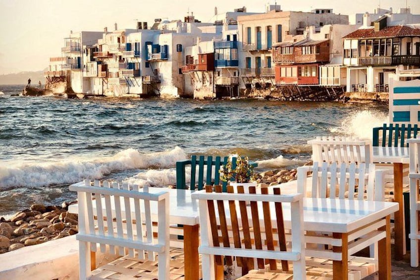 A seaside view with white buildings, a rocky shoreline, and white and green chairs. 2
