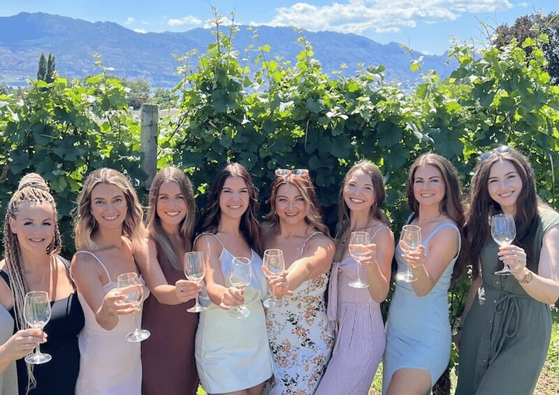 Un grupo de mujeres sosteniendo copas de vino en un viñedo con montañas al fondo. 2