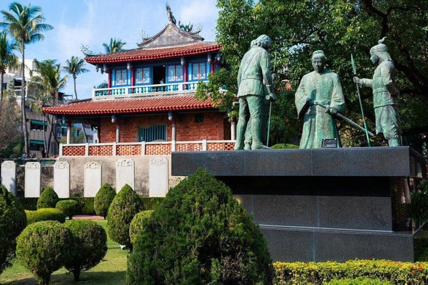 Un bâtiment traditionnel avec un toit rouge, entouré de statues et de buissons bien entretenus. 3