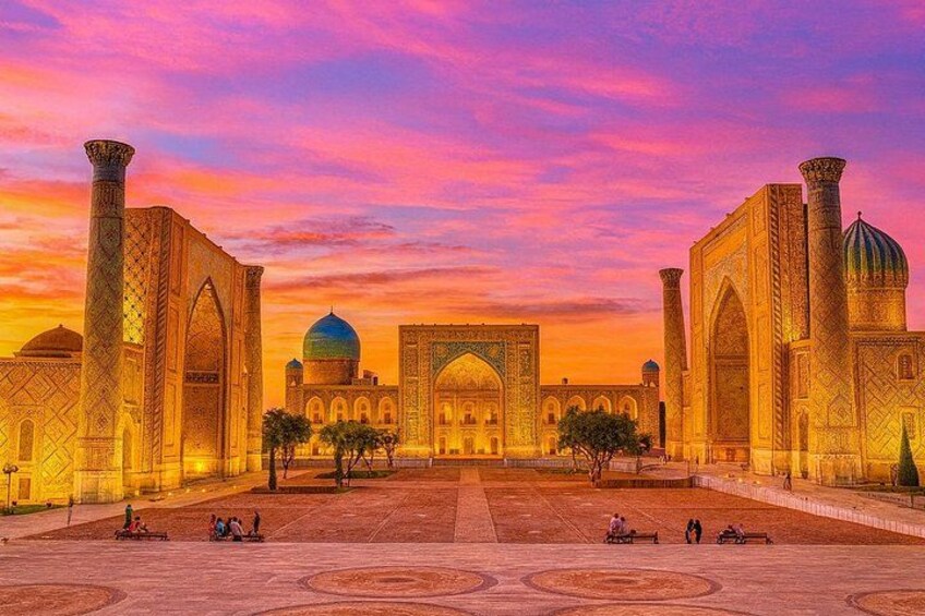 A historic building with domes and arches, surrounded by a courtyard with people. 1