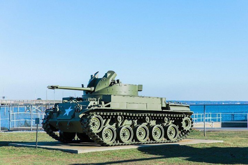 A military tank on display with a blue sky and a fence in the background. 2