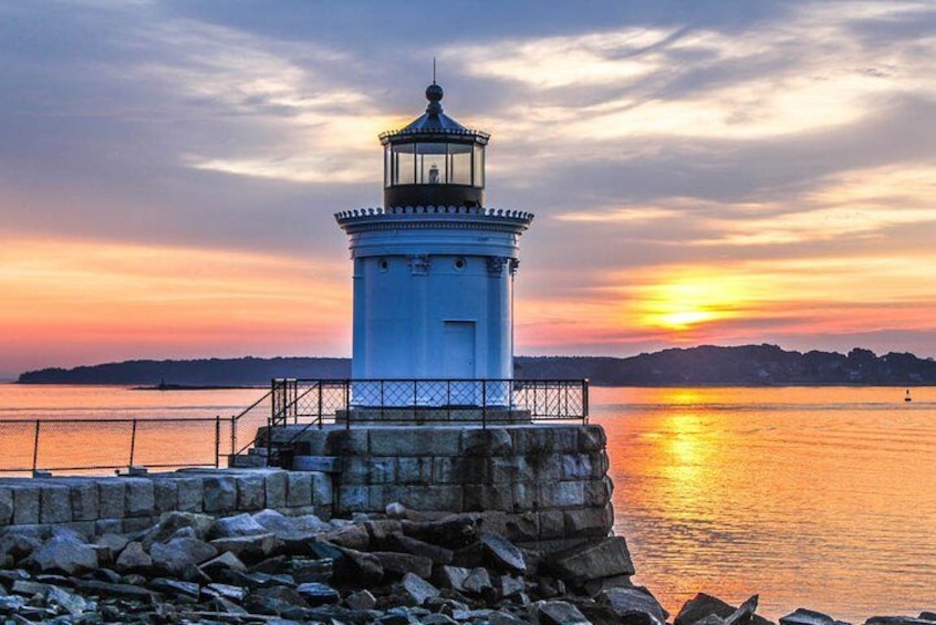 A lighthouse at sunset with a rocky shoreline and calm water. 2