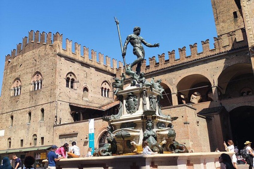 Ein historisches Gebäude mit einer großen Statue auf einem Brunnen, Touristen in der Nähe und einem strahlend blauen Himmel. 1