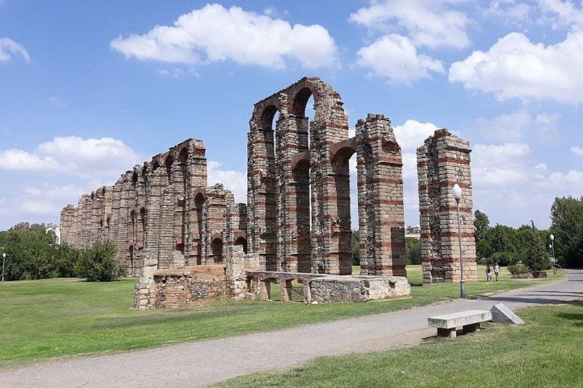Ancient ruins with arches and columns, surrounded by a grassy area and a paved path. 1